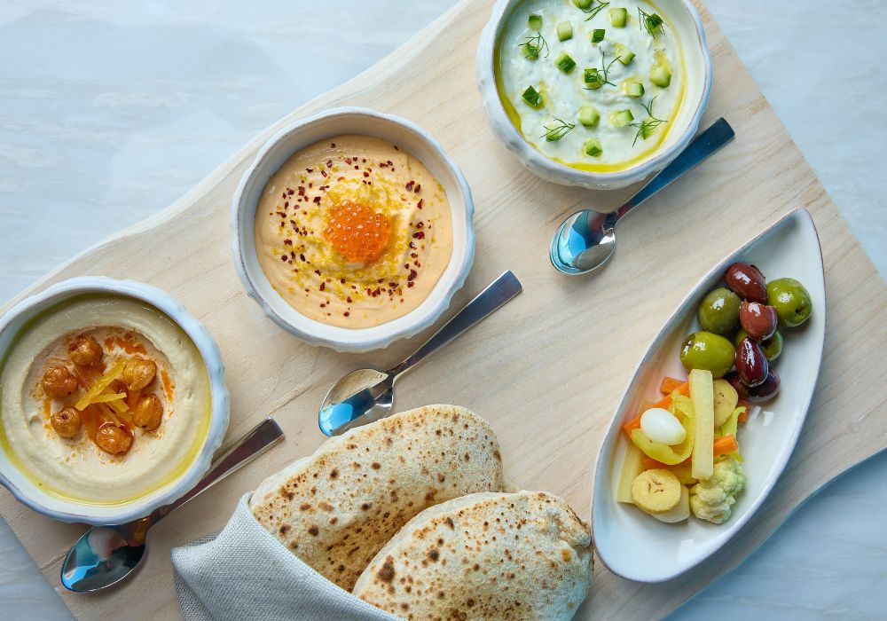 Variety of dip plates and olives on wooden tray 