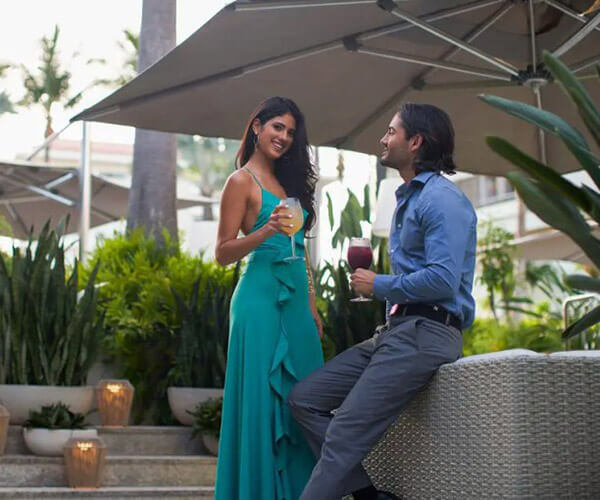 Couple in semi-formal attire relaxing together under a patio umbrella with wine