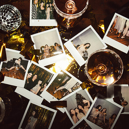 Polaroid photos laid haphazardly on a table with gold confetti, a mini disco ball, and drinks in coupe glasses